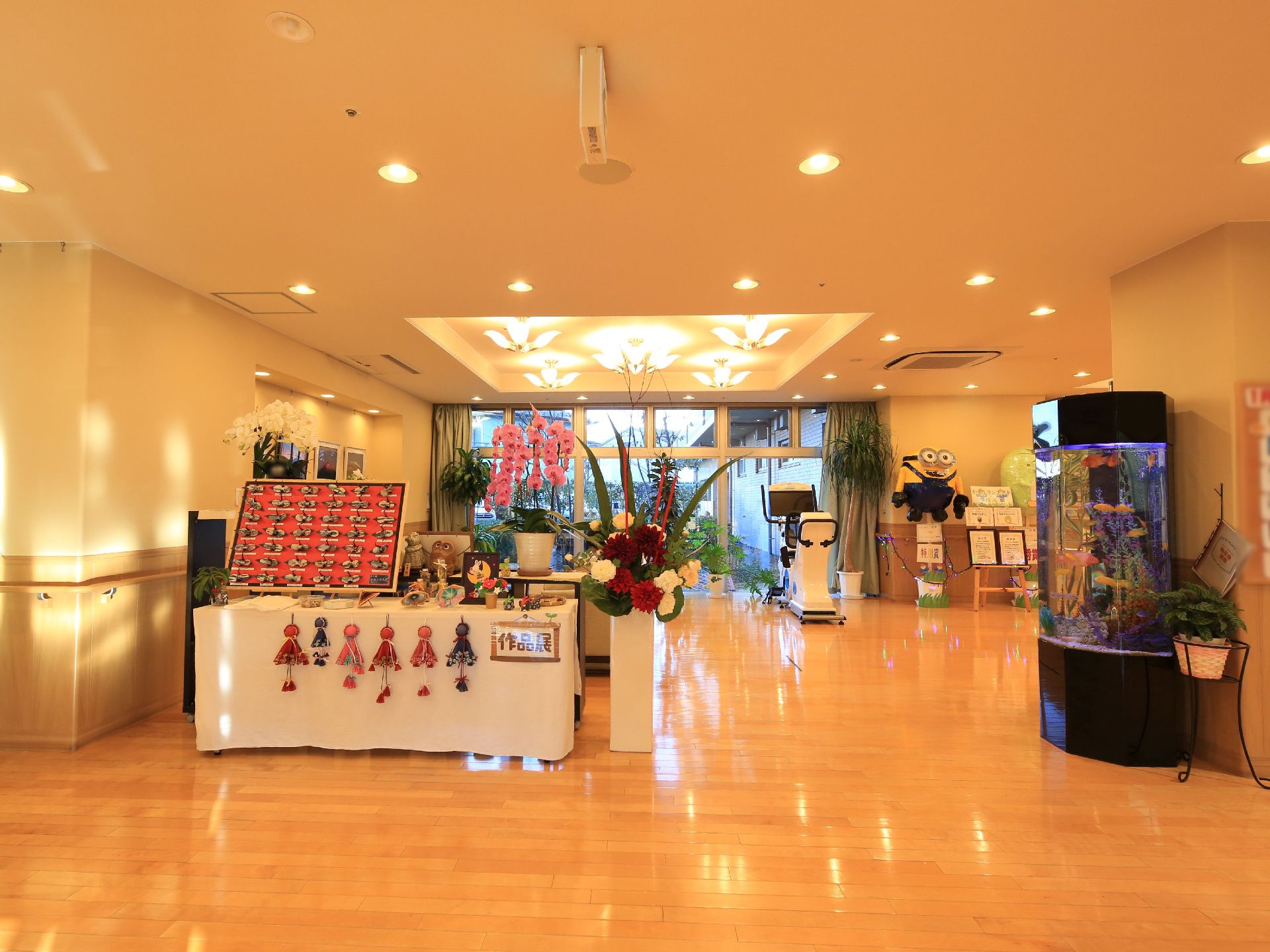 大きな水槽のある玄関ホール。奥の方には大きな窓がある。作品展と看板が掛けられた台があり、折り紙や手作りの作品が並べられている。