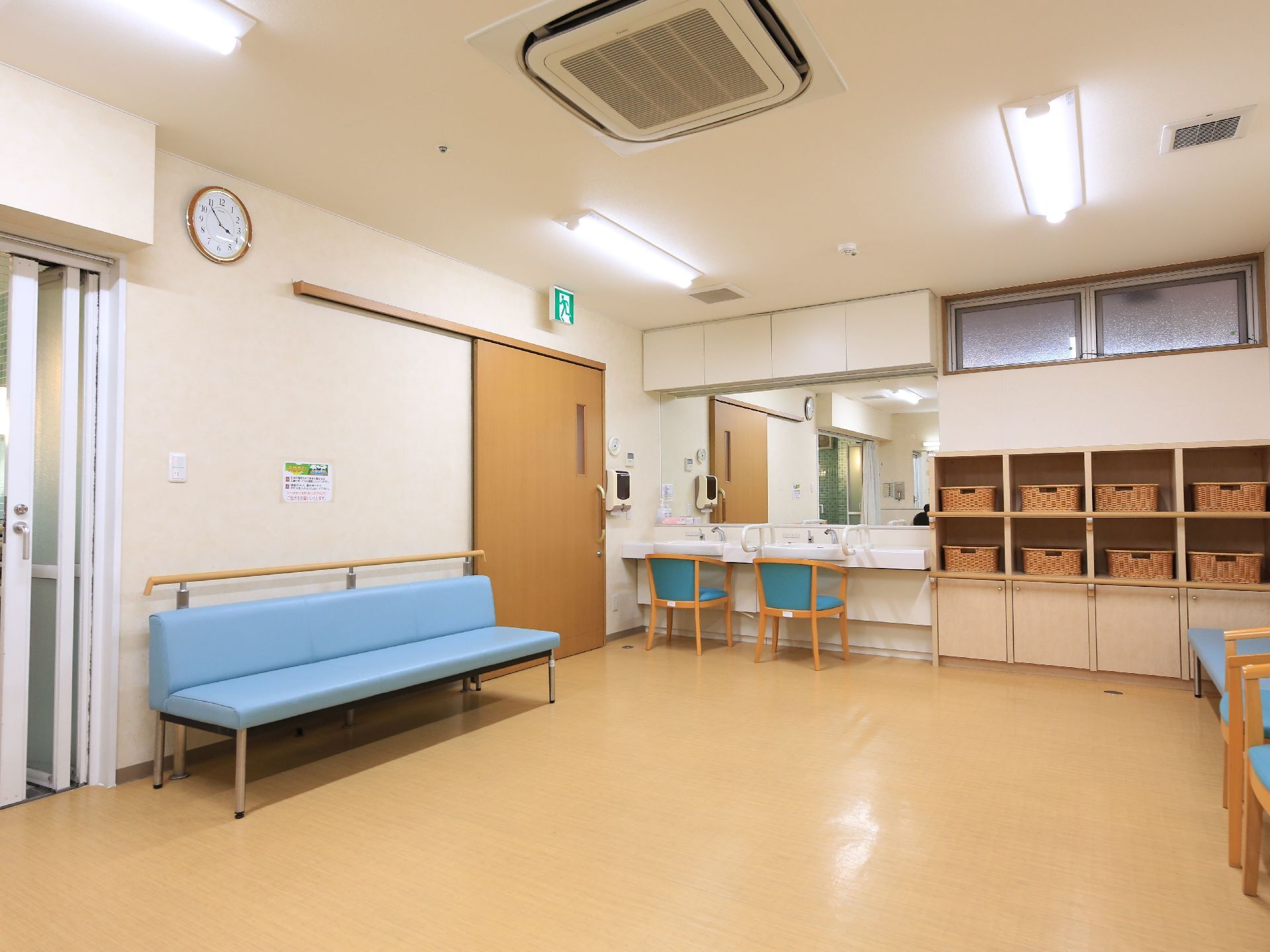 広い脱衣所がある。壁には洋服を入れるかごが置かれた棚がある。洗面台が二台と鏡があり、水色のベンチと椅子が置かれている。