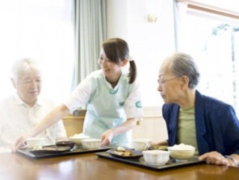 座っている入居者に、食事のトレーを配膳するスタッフ