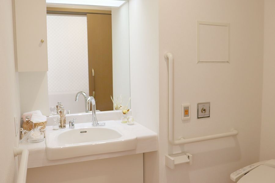 白を基調とした清潔感のあるトイレである。トイレカバーやスリッパはクローバーの模様で統一されている。洗面台には観葉植物が飾られている。