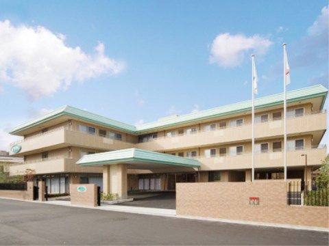 薄いグリーンの屋根にクリーム色の壁をした、L字型で3階建ての施設