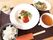 赤いソースとハーブが添えられたメイン料理に白いご飯、スープ、サラダ、フルーツが添えられたヨーグルトのようなデザートがある。