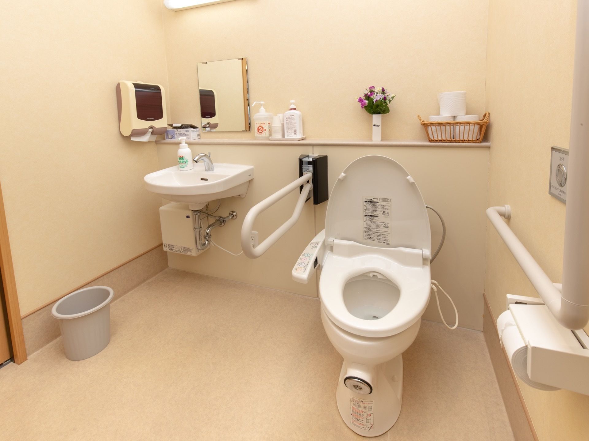 便器のとなりに手洗い場が設置されているトイレである。便器のそばには可動式、壁には備えつけの手すりがついている。