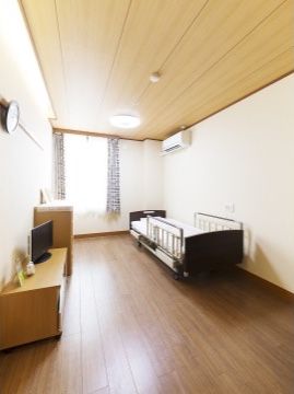 シンプルな介護用ベッド、テレビ、チェスト、時計などが置いてある居室。エアコンも設置されているため、温度調節も可能になっている。