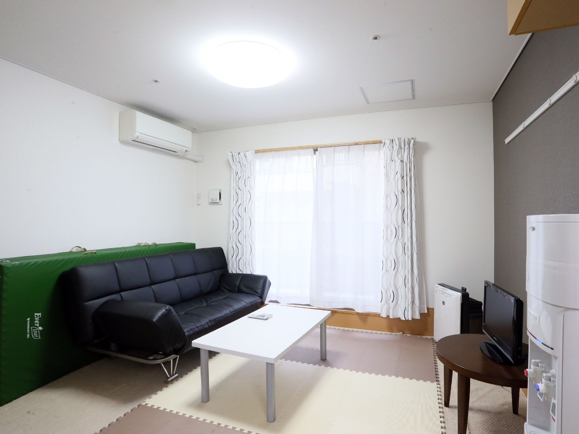 部屋には、大きな黒いソファーが置かれている。そして、ソファーの前にはテレビがあり、白いテーブルも置いてある。