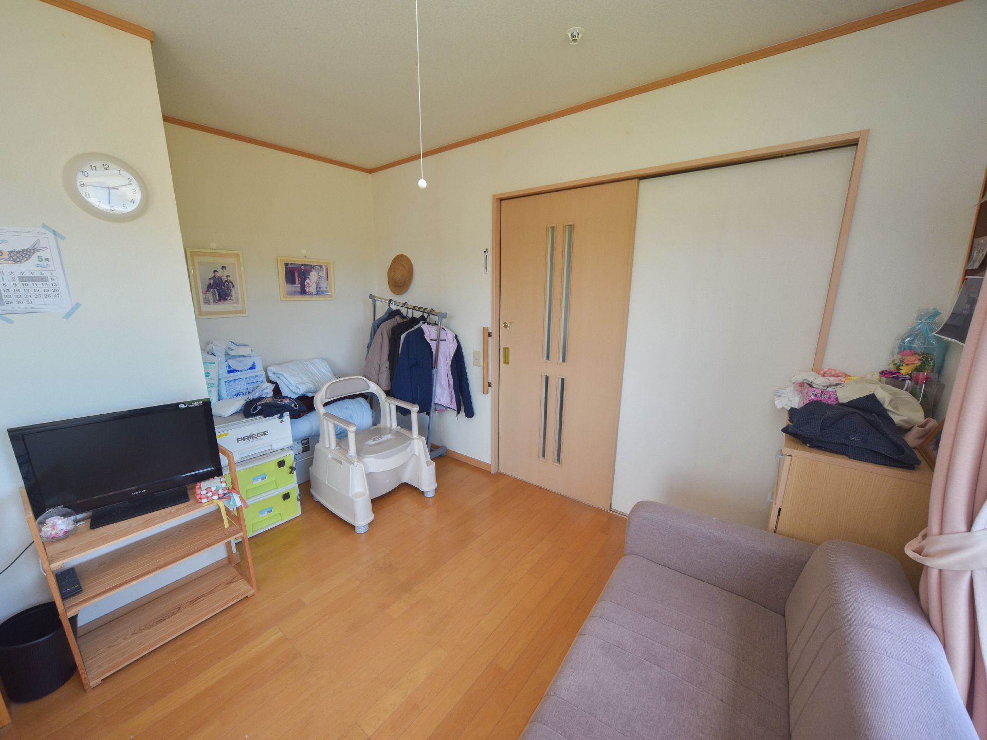 個室の奥には、取っ手のついた木製のドアがある。左側には時計やテレビ、さらに奥まったところには家族写真などが貼られている。