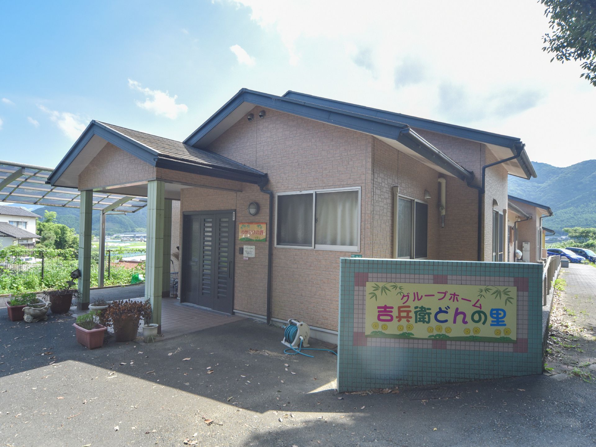 右手前には、施設名が書かれた大きめの看板が目立つ形で掲示されている。施設周辺には山々がそびえたっている。