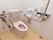 白色とベージュ色の内装のトイレである。便器の後部に背もたれ、両側には手すりを取り付けている。便器のすぐ横の壁には小さな洗面を設置している。