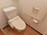白色の壁と木目の床のトイレである。横側の壁にはエル型の手すりとナースコール、トイレットペーパーホルダーを設置している。