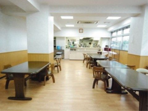 ダークブラウンのテーブルセットが置かれた食堂。奥にあるキッチンでスタッフが働いている。