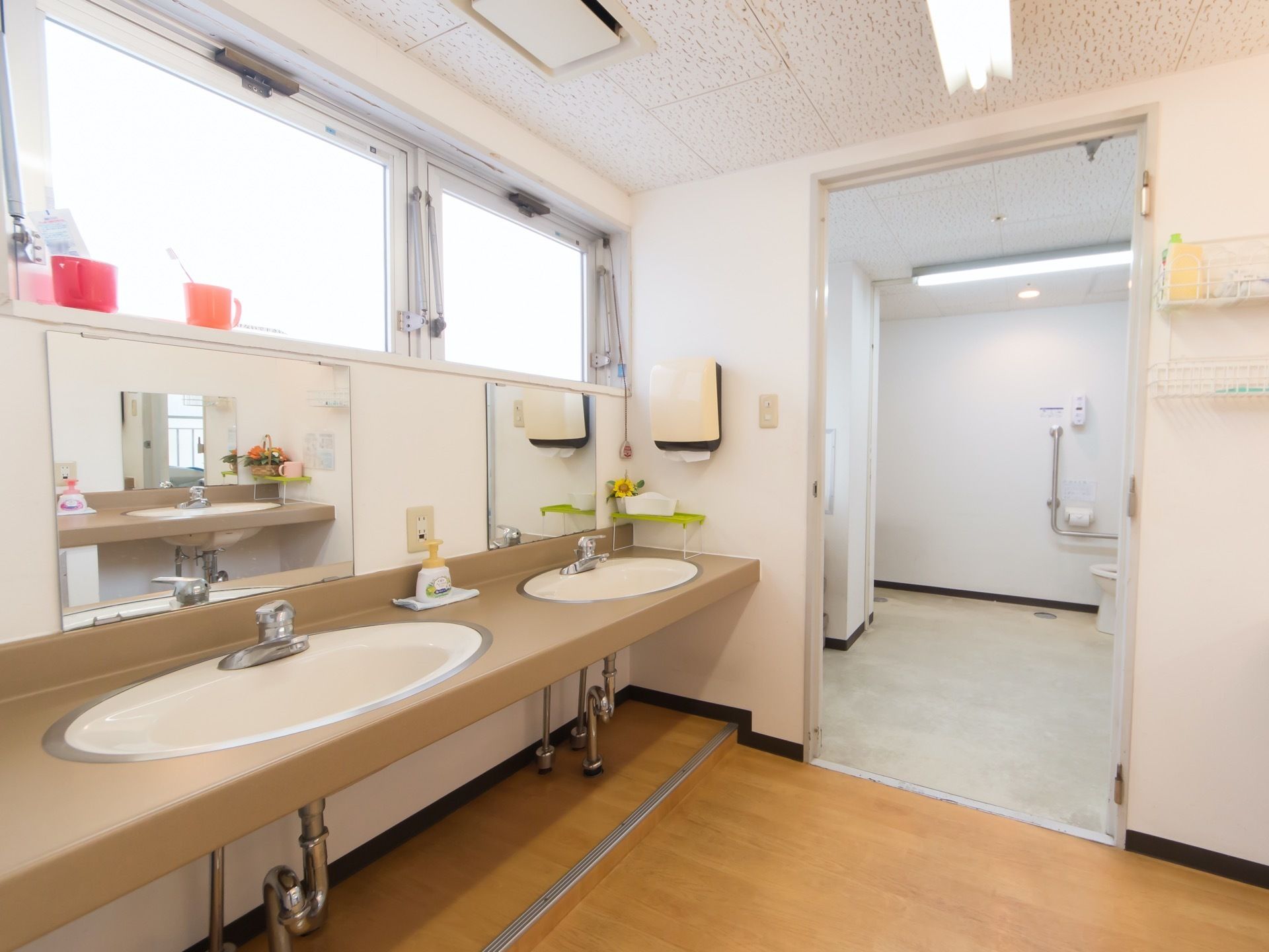 手前に洗面台が二つ並んでおり、その奥に共有トイレがある。洗面台の前には鏡が設置されており、周りにハンドソープや歯磨きセットが置かれている。
