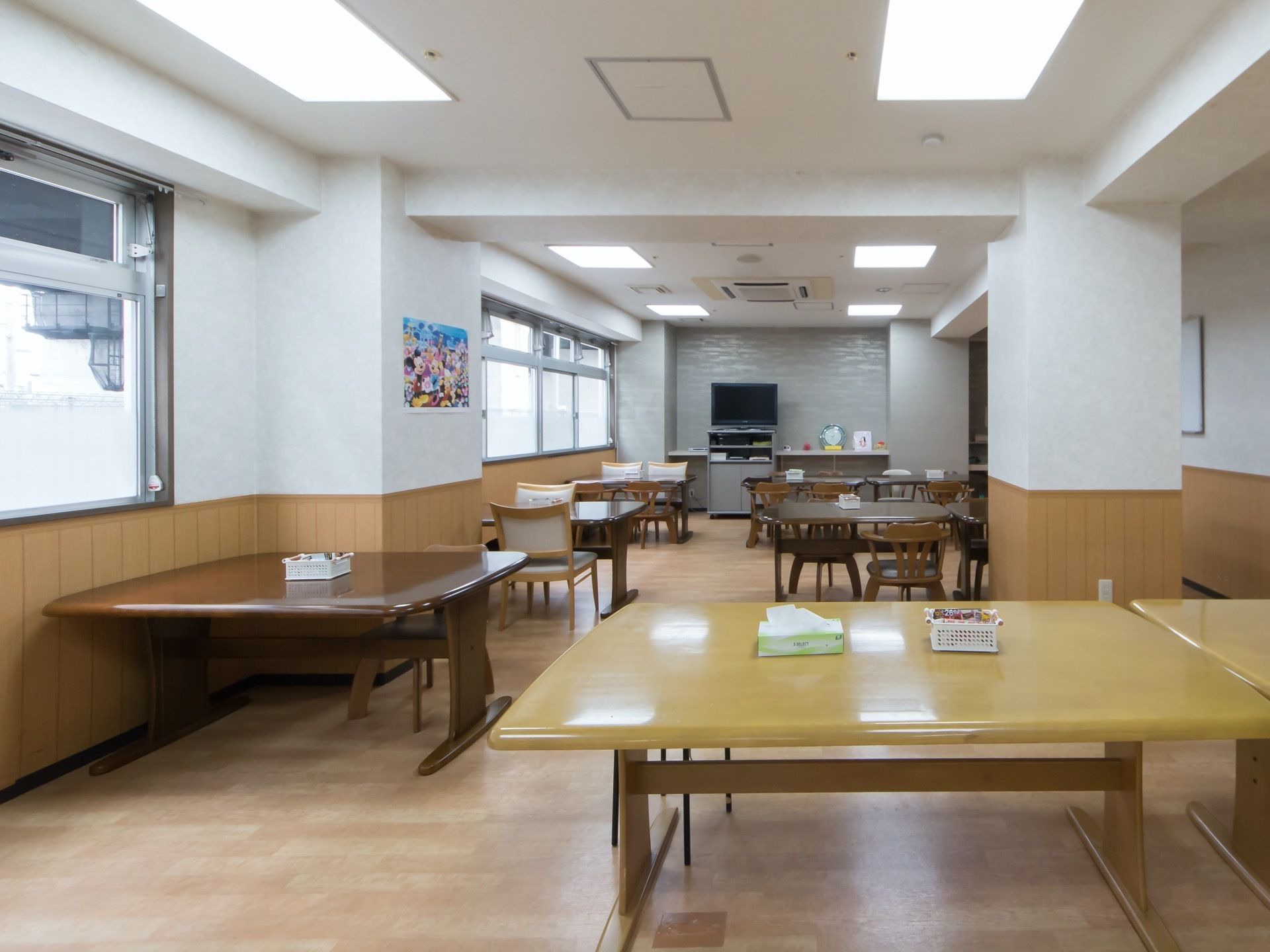 テーブルや椅子など、落ち着いた茶系の家具で揃えられた食堂である。奥の壁際にはテレビが設置されている。