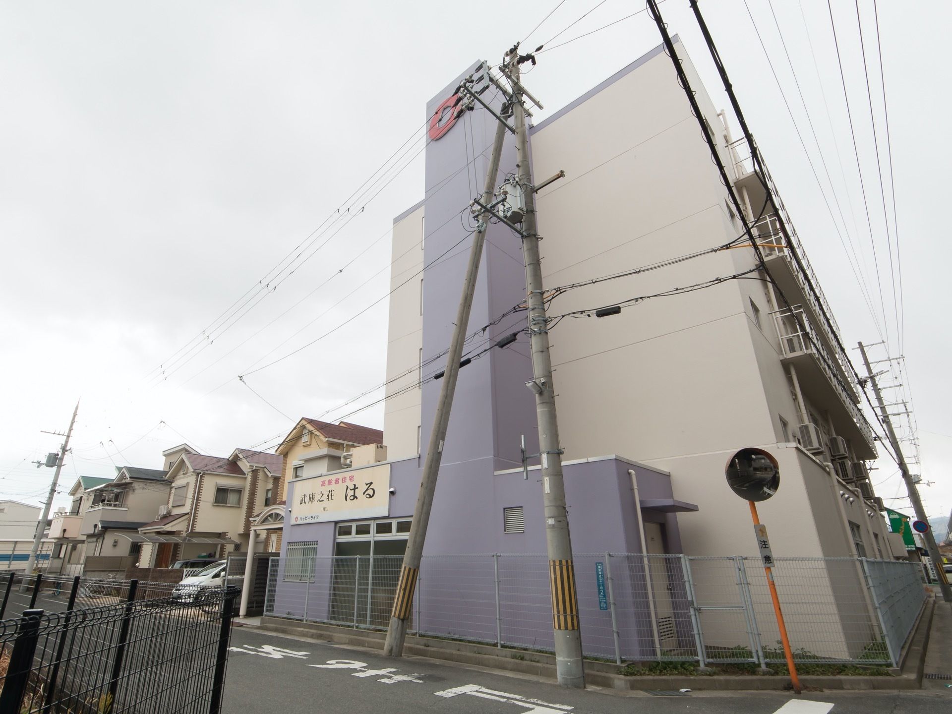 ツートンカラーの外壁で、道路との境目には柵が立っている。手前の壁に、施設名の書かれた大きな看板が付いている。