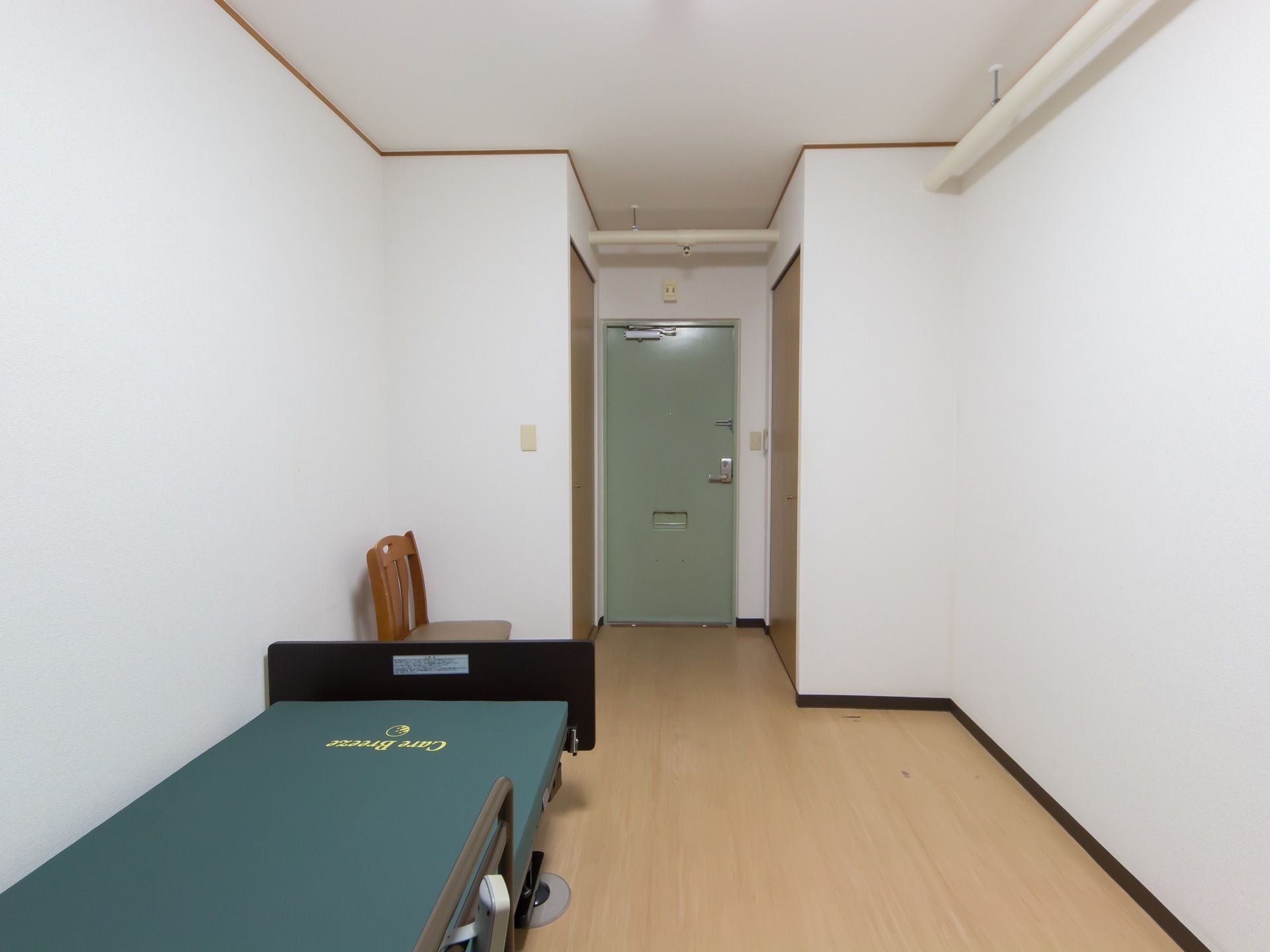 出入り口のドアの左右に、トイレと収納の扉がある。室内には椅子が一脚と、電動介護ベッドが一台置かれている。