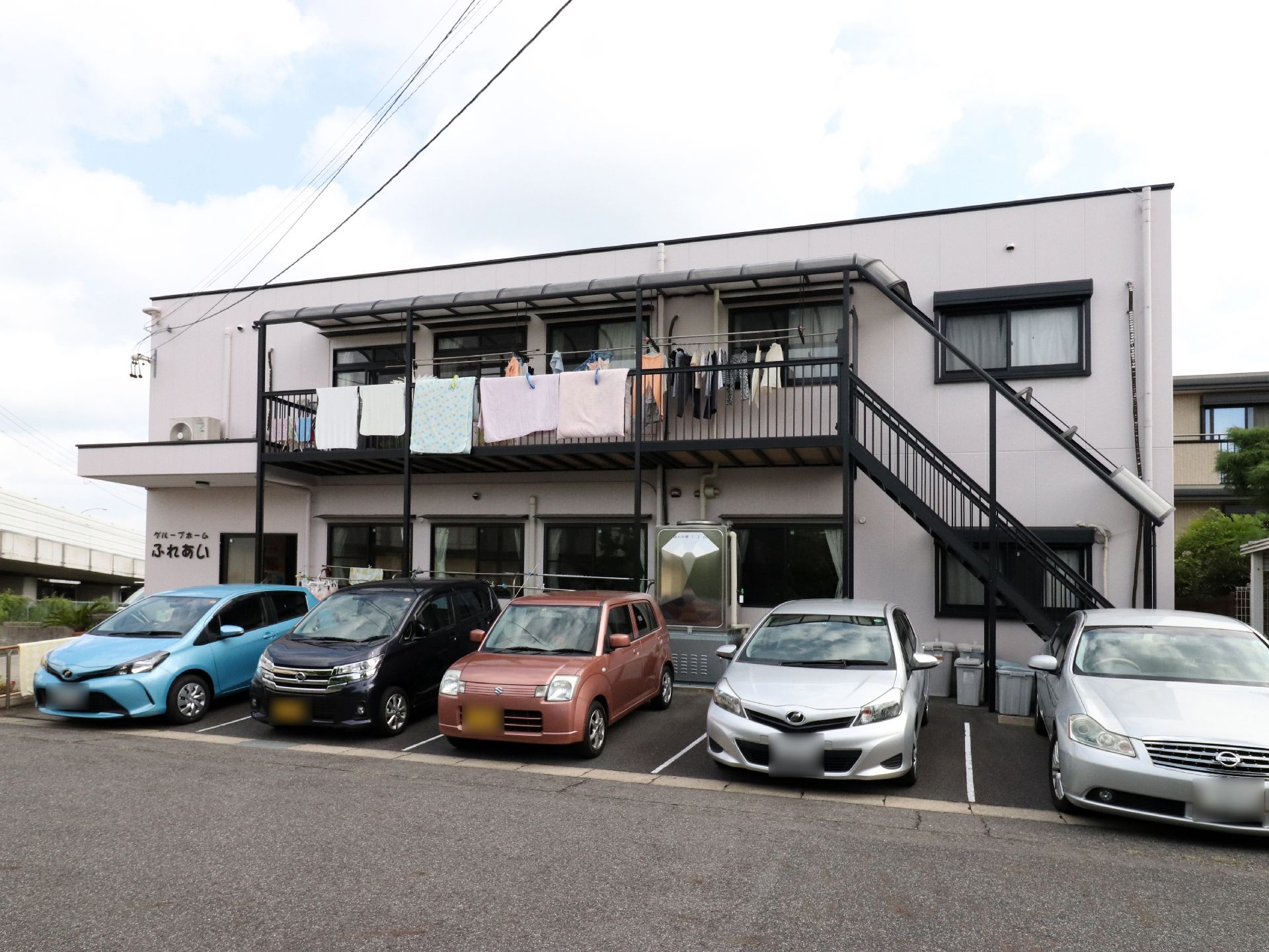 施設の建物は2階建てである。アパート風の四角い建物で、外壁は白色をしている。窓枠と外階段などは、黒色である。