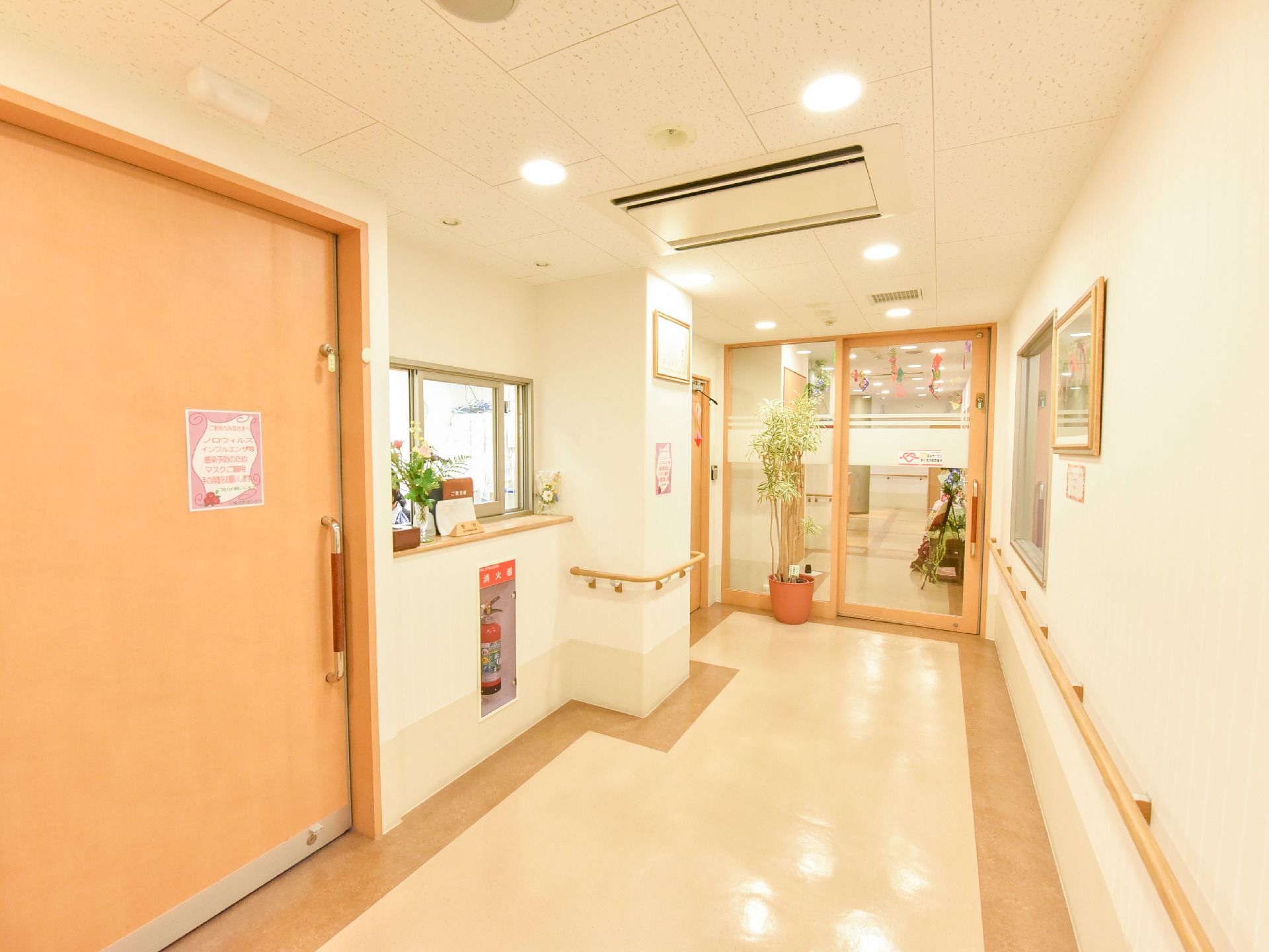 玄関の通路は広く作られている。左手には受付の窓口が設置されている。壁には消火器があり、事務所への扉などもあるのが見える。