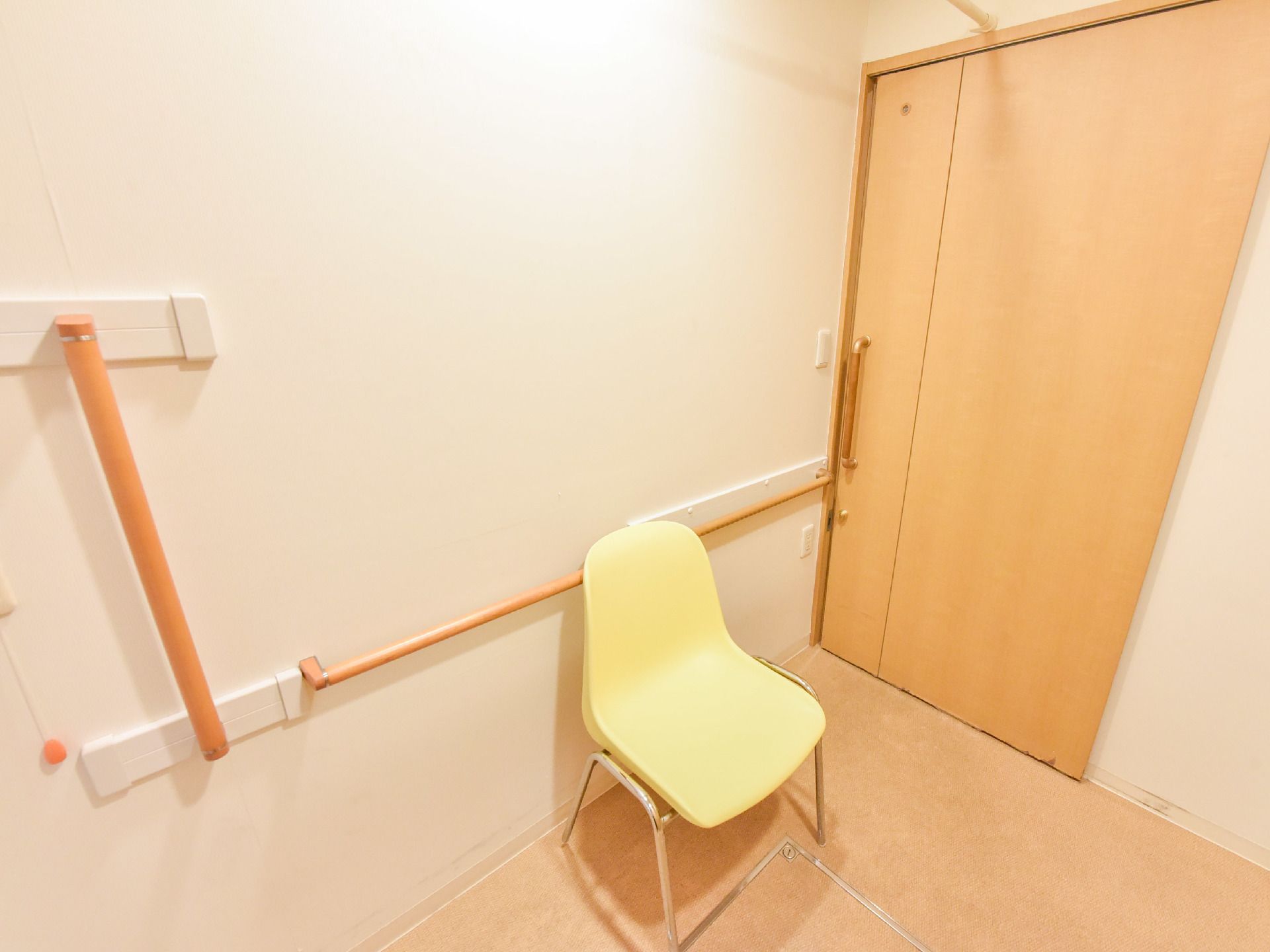 部屋の中に白い椅子が置かれている。椅子の後ろと横に手すりが設置されている。壁は白で手すりが木なので優しい雰囲気。