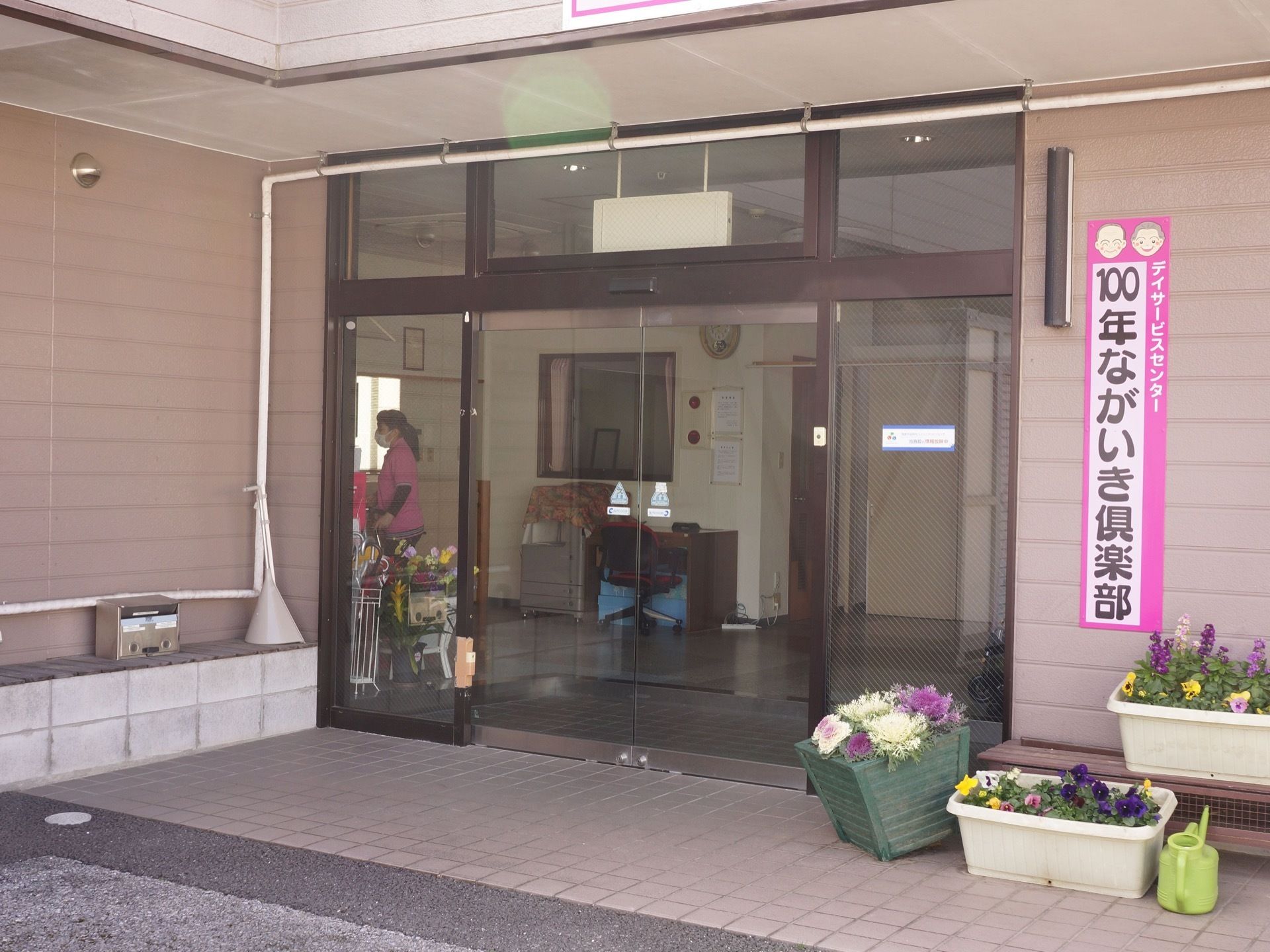 建物入口は大きく開く、ガラスの自動ドアになっている。入口前には段差がなく、沢山の花が植えられた鉢植えが複数置かれている。