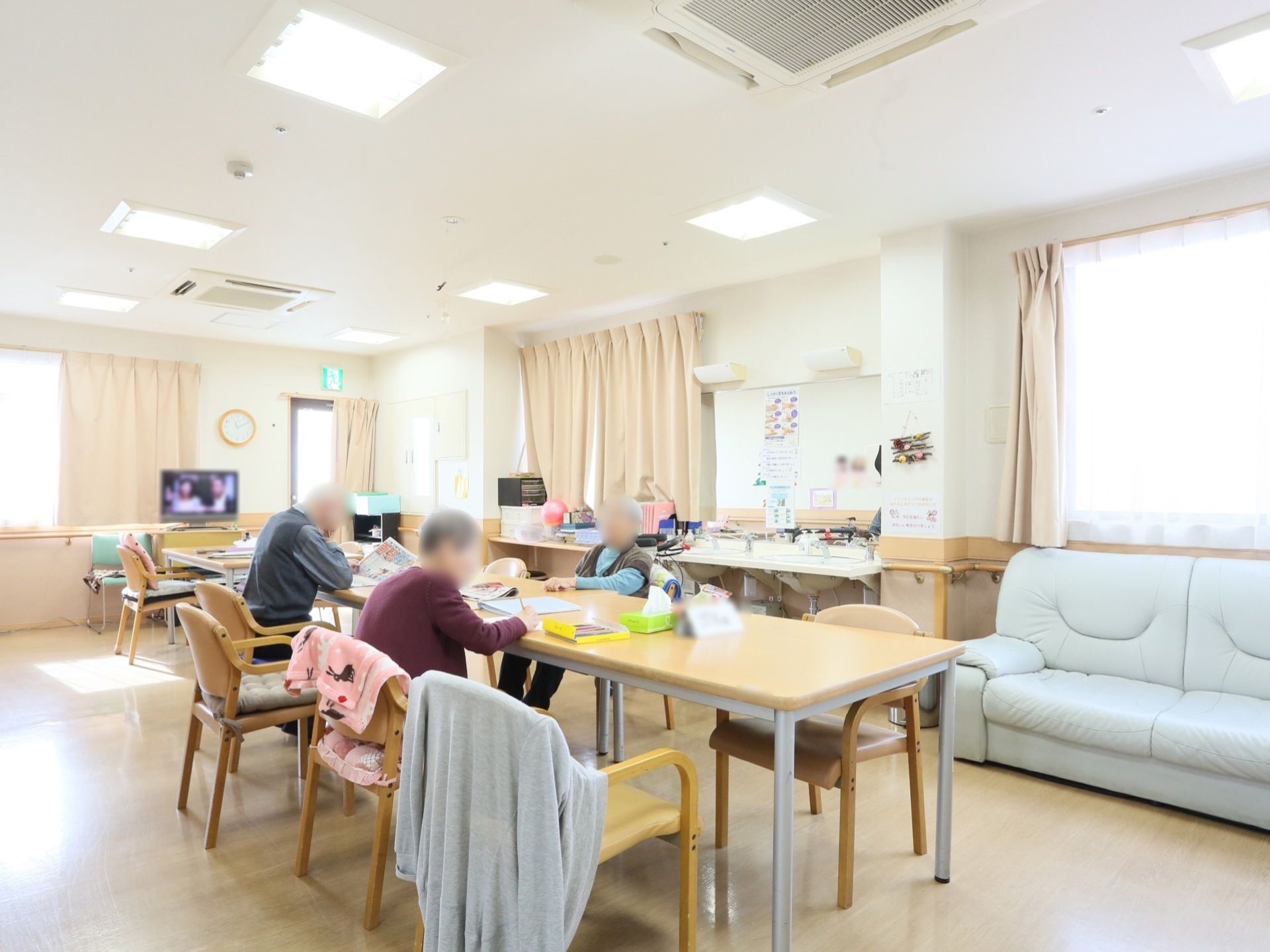 長いテーブルに椅子が置かれた共有スペースである。窓からは明るい日差しが入り、開放的な空間となっている。