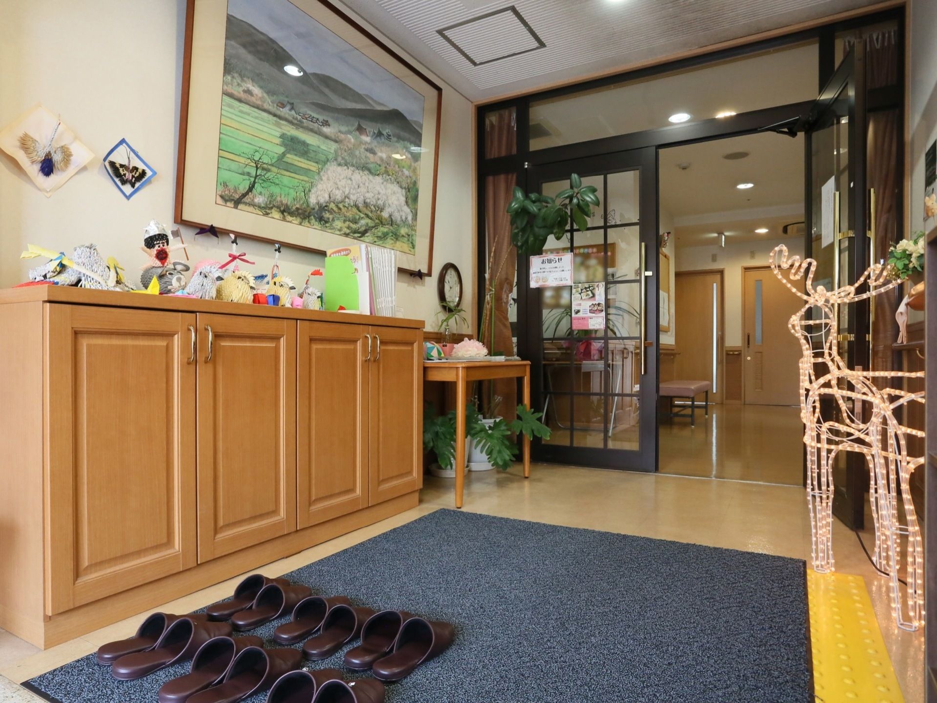 玄関扉は開き戸になっている。左には下駄箱があり、床には多数のスリッパが並べられている。季節のインテリアが飾られている。