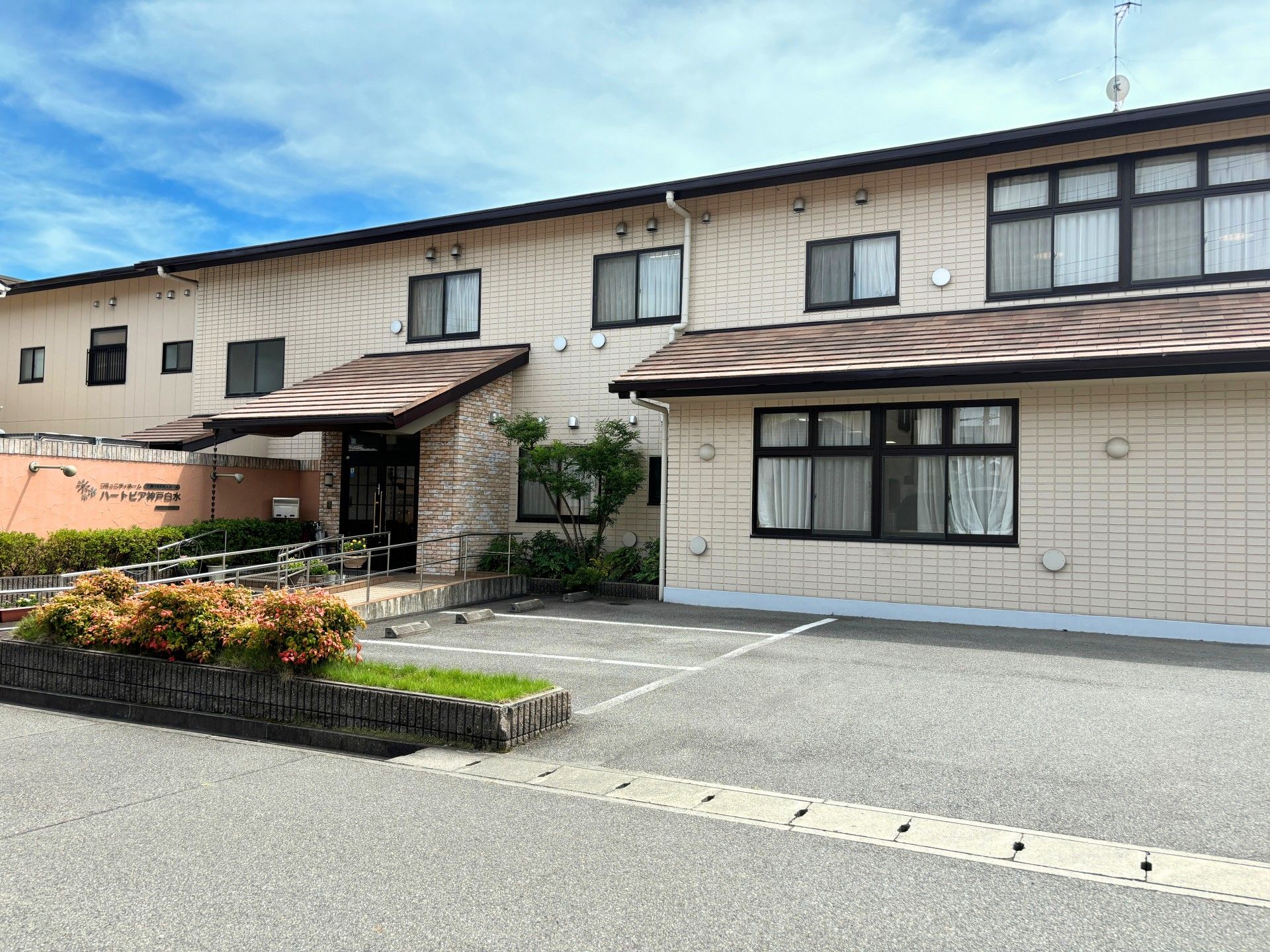 玄関前には植栽やプランターの花などが施されており、あたたかい雰囲気である。幅の広いスロープと段差の小さい階段が付いている。