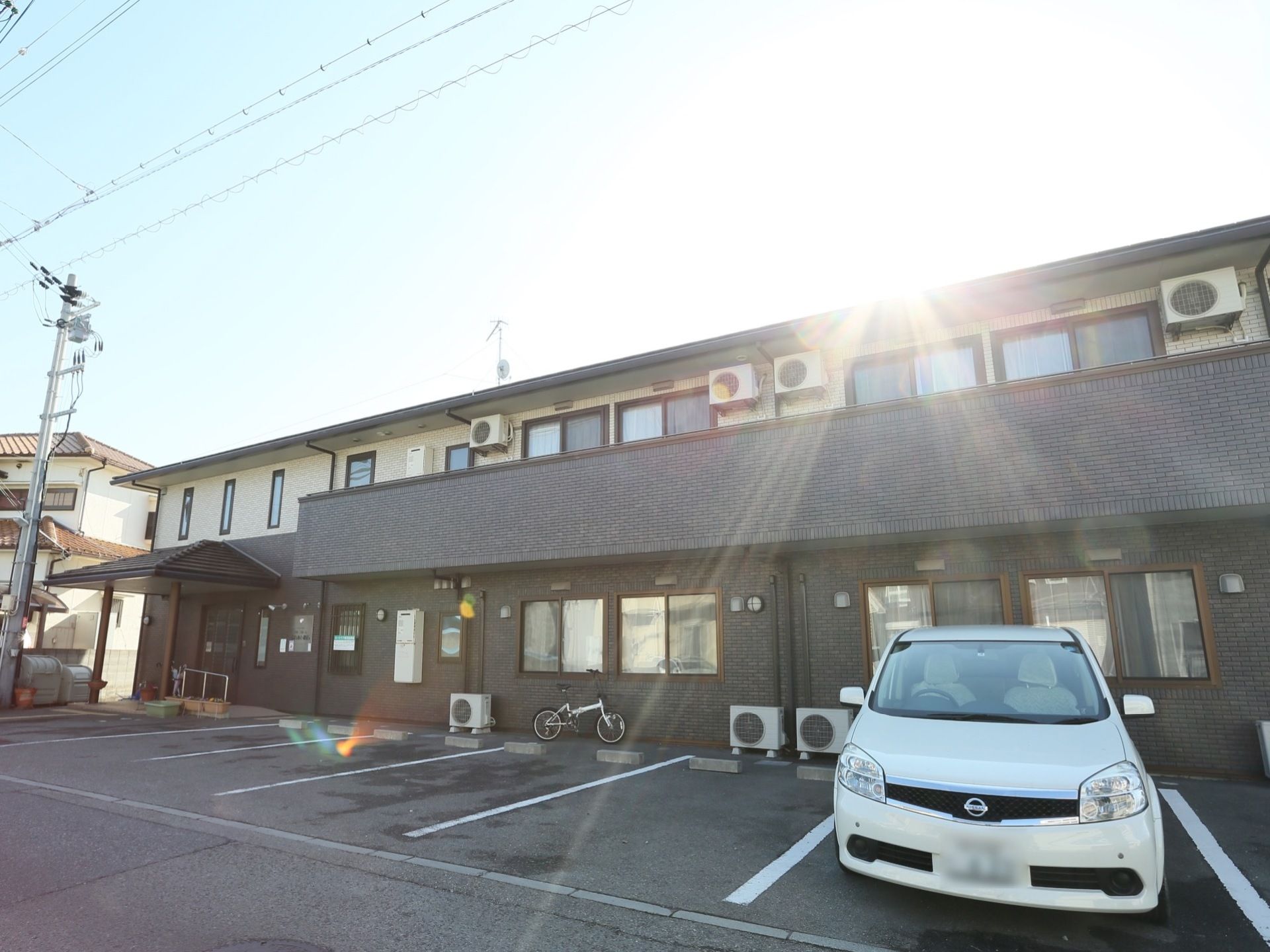 ツートンカラーが印象的な2階建ての集合住宅のような外観。エントランスのすぐそばに駐車スペースが設けられた機能的な造りになっている。