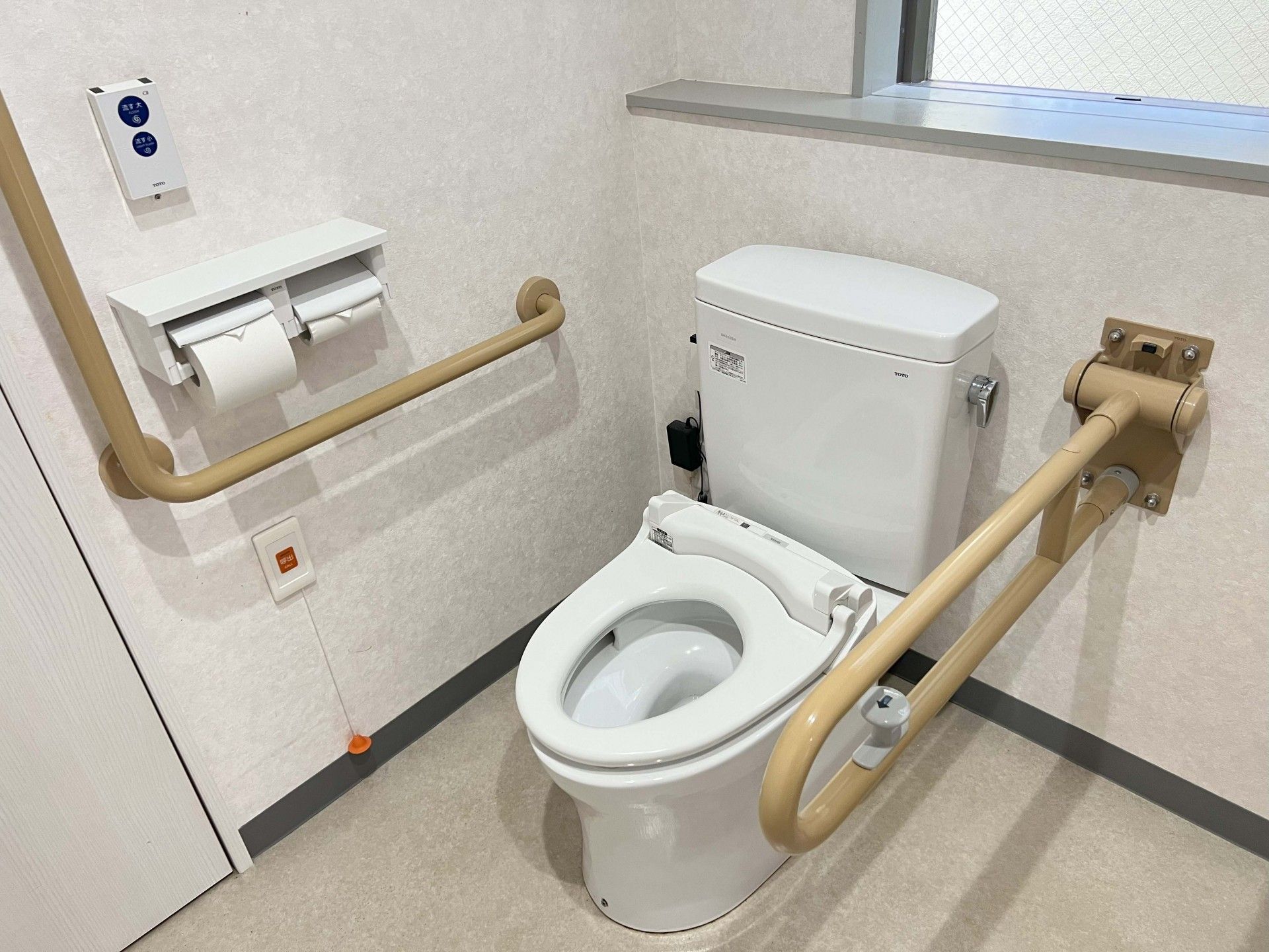 換気窓が設置され明るいトイレの上部には収納スペースが設けられ、壁には手すりや呼び出しブザーが取りつけられている。