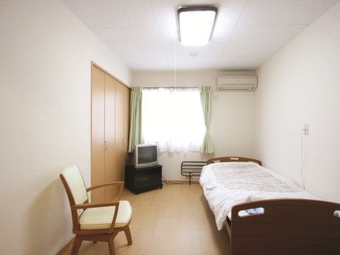 介護機能付きのベッドや椅子、テレビなどが備えられた居室である。空間奥の窓からは十分な明るさが得られるほか、収納スペースも確保されている。