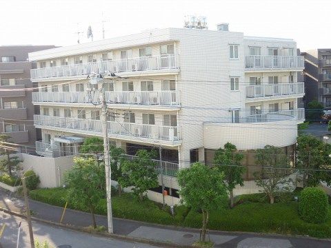 周囲に剪定された生垣や木々が植えられている白い外壁の5階建ての建物