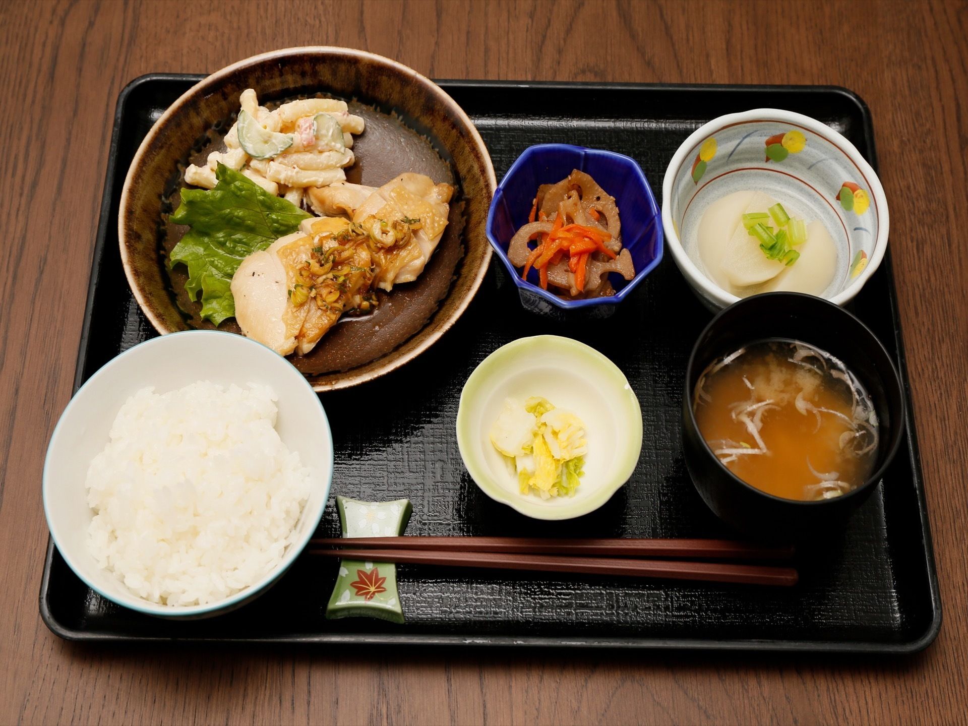 テーブルに置かれた黒いお盆の上には、おいしそうな食事が並べられている。手元には、箸が添えられている。