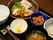 黒いトレーの上には、器に盛りつけられた6種類の料理が並んでいる。大皿には、鶏肉料理とマカロニサラダが盛られている。