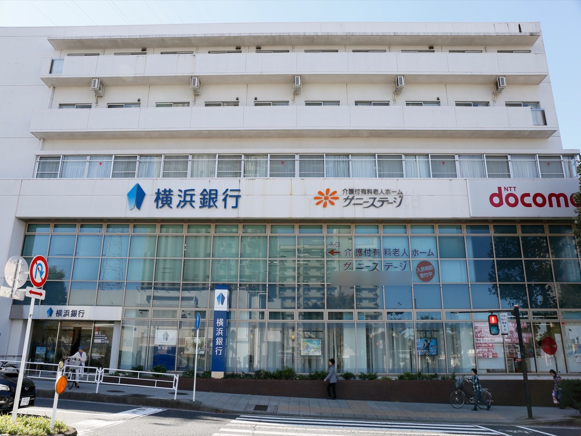 施設の外観は、他の企業と隣り合った形となっている。複数階建ての建物となっており、地上の道路部分に人が歩いている。