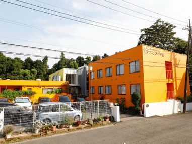 施設の建物は地上2階、地下1階建て。オレンジ色の外壁はとても目立つ。建物の手前は駐車場になっている。