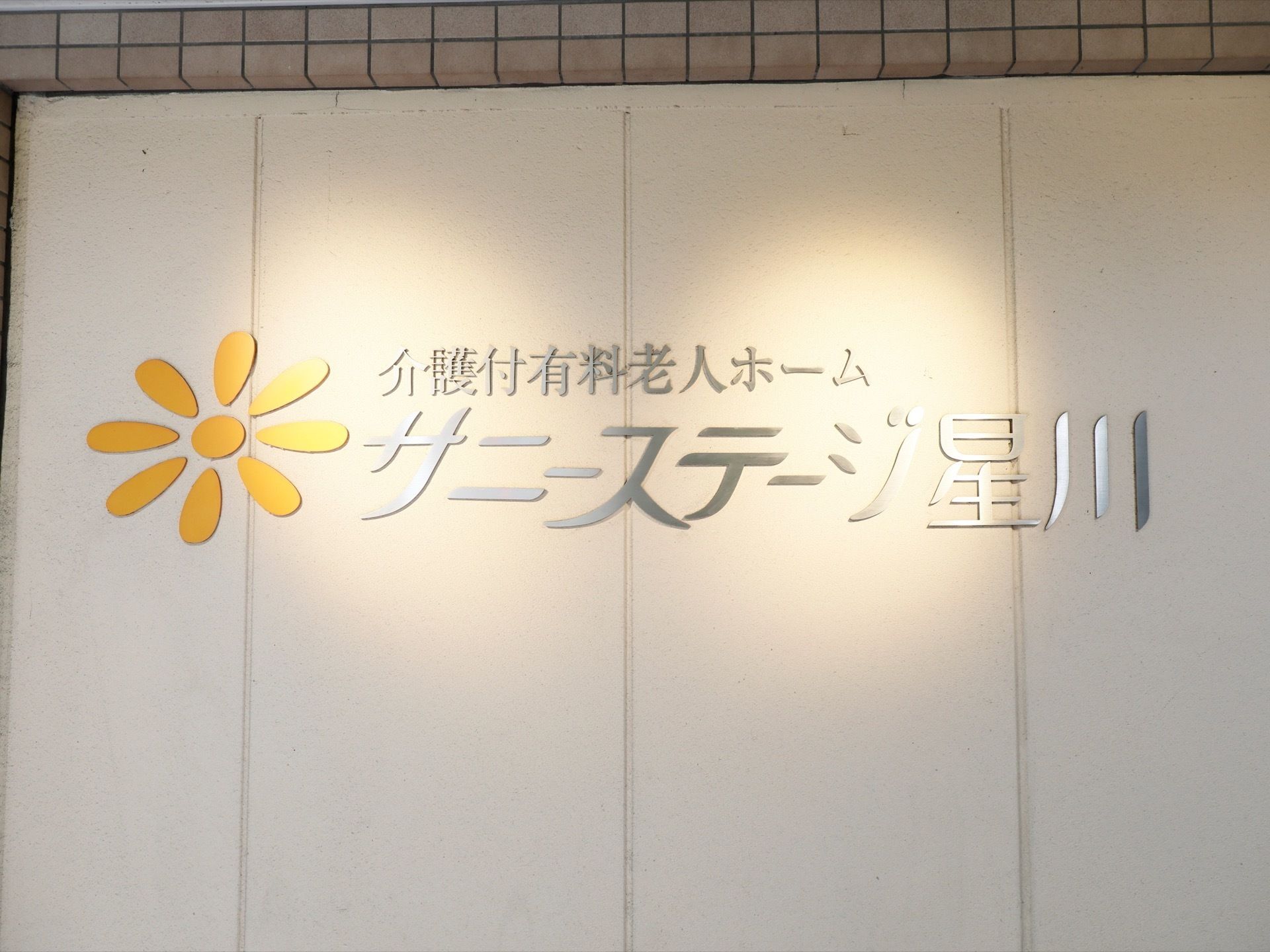 看板に施設名が表示されている。文字の部分に灯りをあててライトアップされている。施設のシンボルマークも一緒に表示されている。