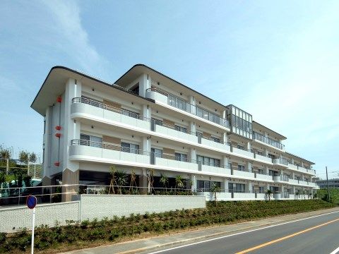 道路に面し、塀と建物の外壁が真っ白な３階建て施設の外観