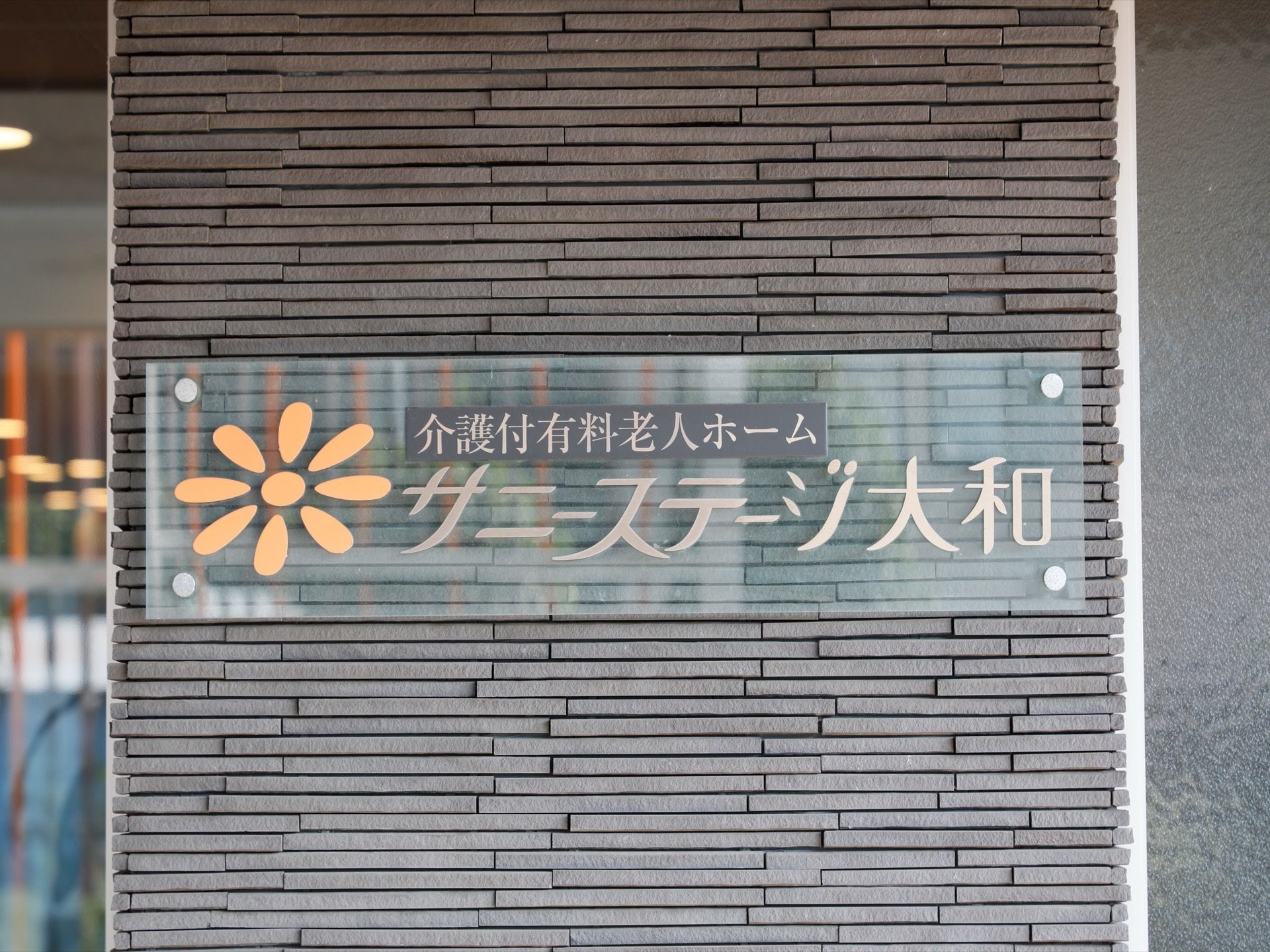 玄関横に取り付けられている看板はおしゃれなガラス製。大きな施設名とマークが書かれている。目立った看板。