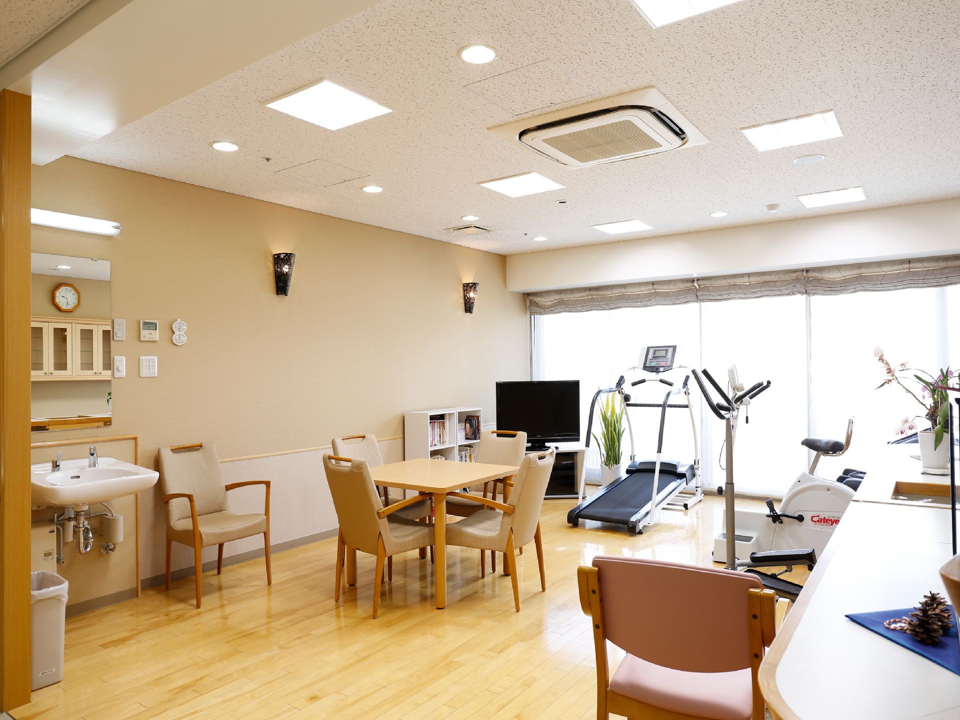 内装は、茶と白のコンビネーションの壁、白い天井、木目の床、一面のガラス戸。テーブルやイス、テレビ、本棚、そして機能訓練機材などが設置。