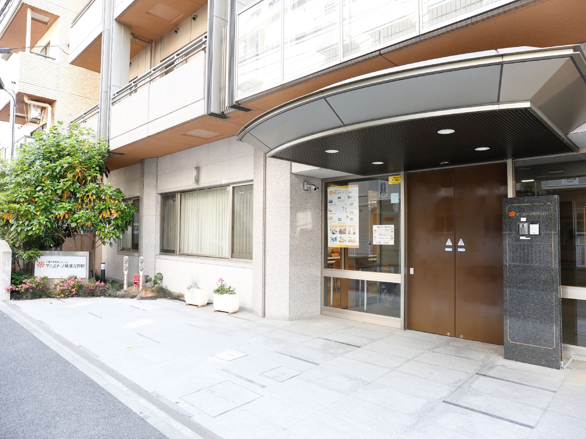 焦げ茶のドアに黒い厚みのある屋根でどっしり感があるエントランス。ドアの両側はガラス張りで、玄関の前は、石畳のスペース。