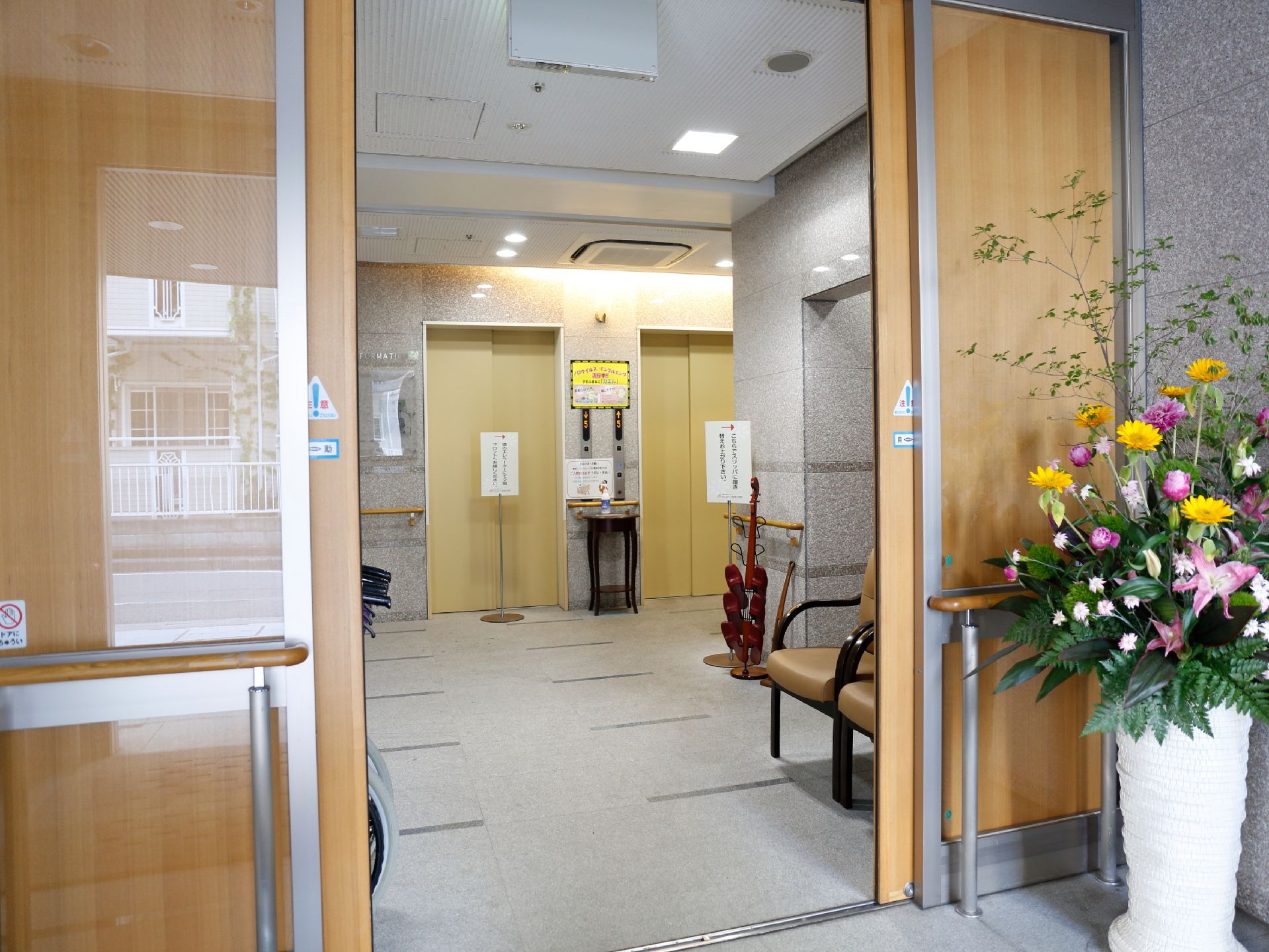 入口ドアの横には、大きな生け花が置かれ、中に入ると、右側には、2つの椅子が並べてある。正面は、エレベーターが2ヶ所設置してある。