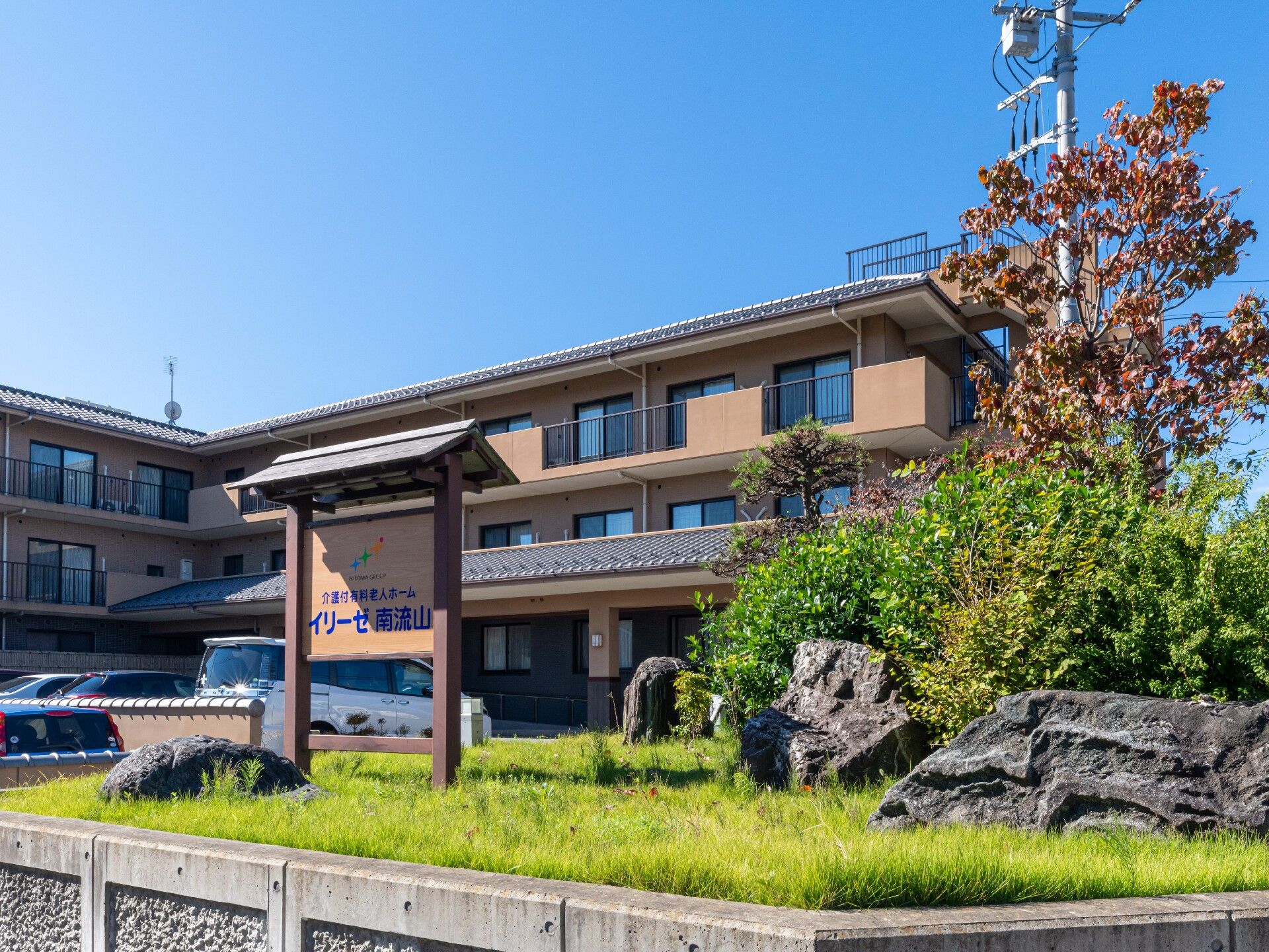 施設の外観は和風で、施設名が表示された看板も和風である。看板のフォントは行書体である。看板の近くには松などが植えられている。