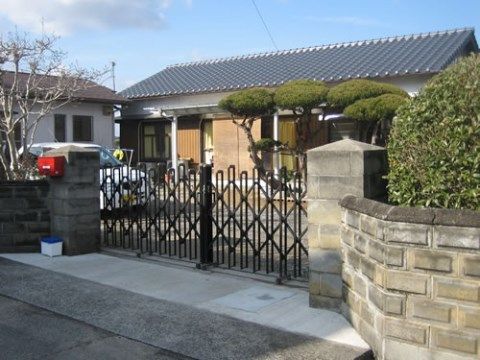 アコーディオン型の門扉に奥に、黒い瓦屋根の建物がある外観
