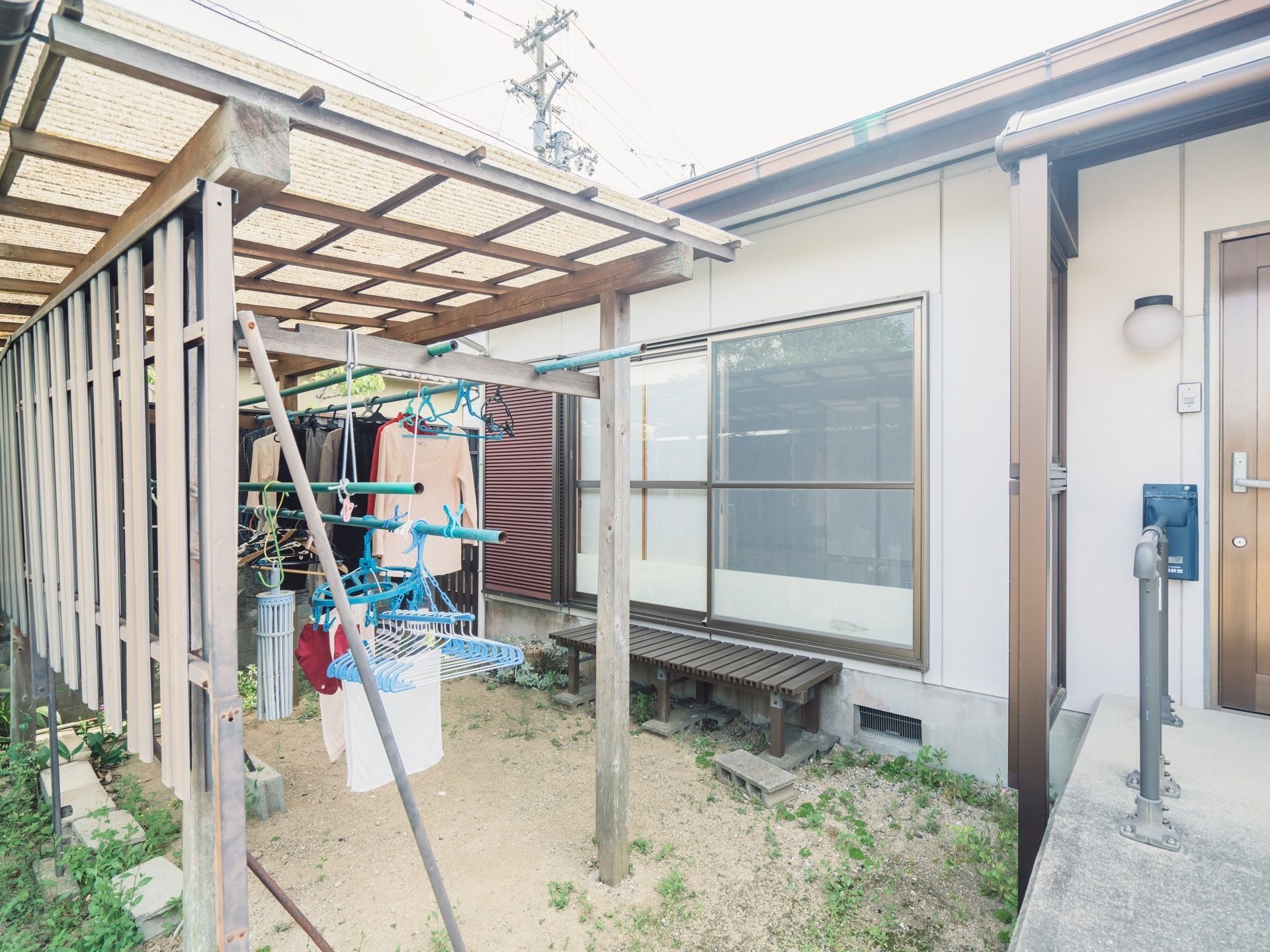 窓の前には縁台が置かれ、庭には屋根付きの洗濯干しスペースがある。玄関ドアの上にはひさしが設置してある。