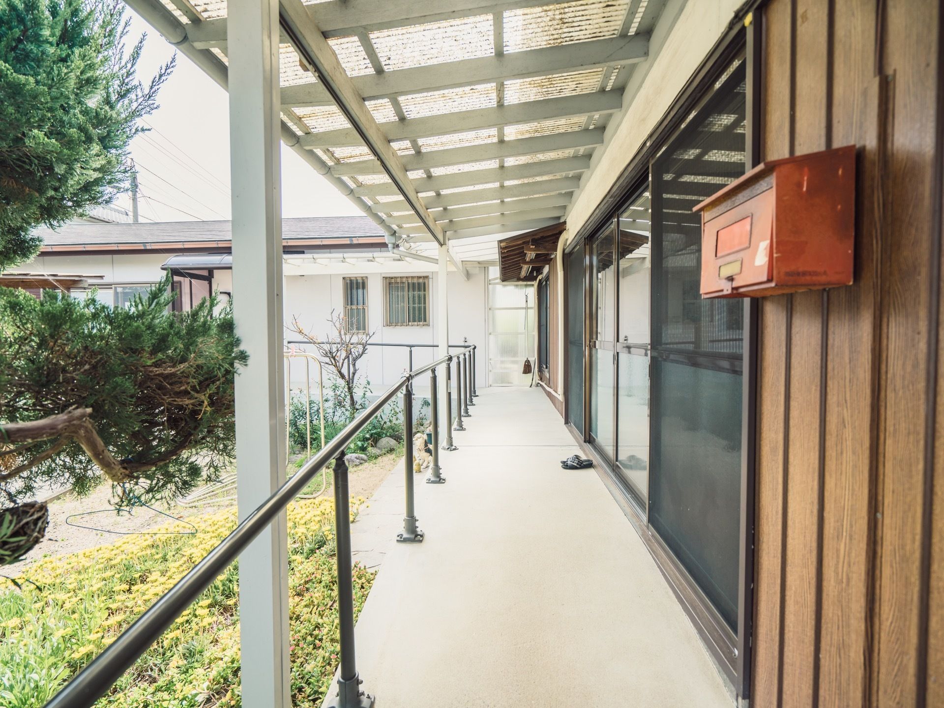 木造平屋建ての施設である。赤色のポストが設置されている。通路には手すりを完備。庭木も植えられている。