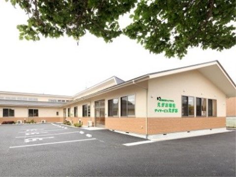 壁に緑色の文字で施設名が書かれ、駐車場が広がる施設外観