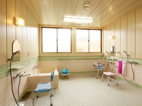 大きな窓が２つついた広々とした浴室。介護用のシャワーチェアは背もたれのついたものとついていないものがそれぞれ用意されている。