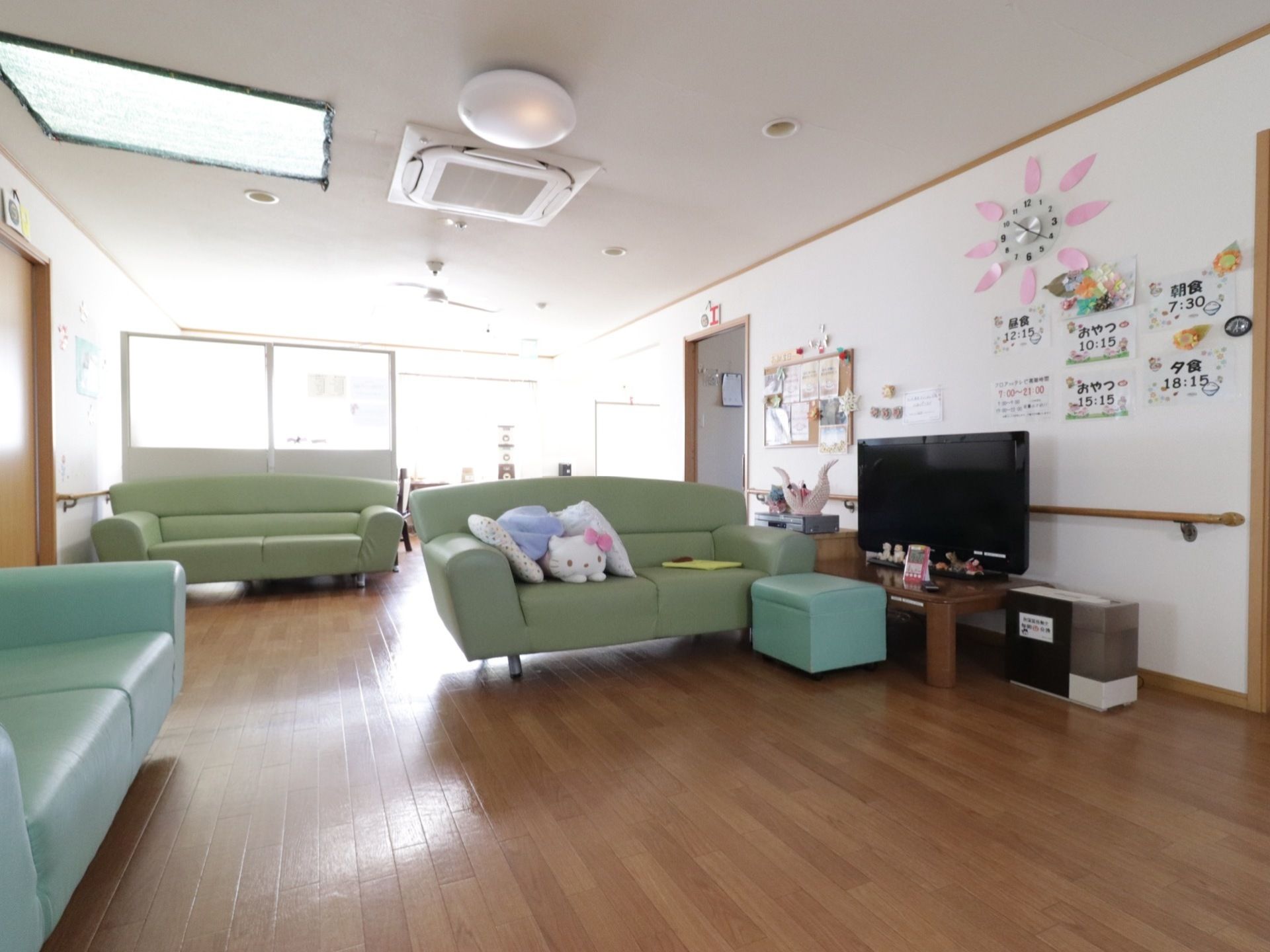 緑色のソファが３台置かれている。大型テレビが設置されている。エアコンが完備されている。壁には時計が掛けられている。