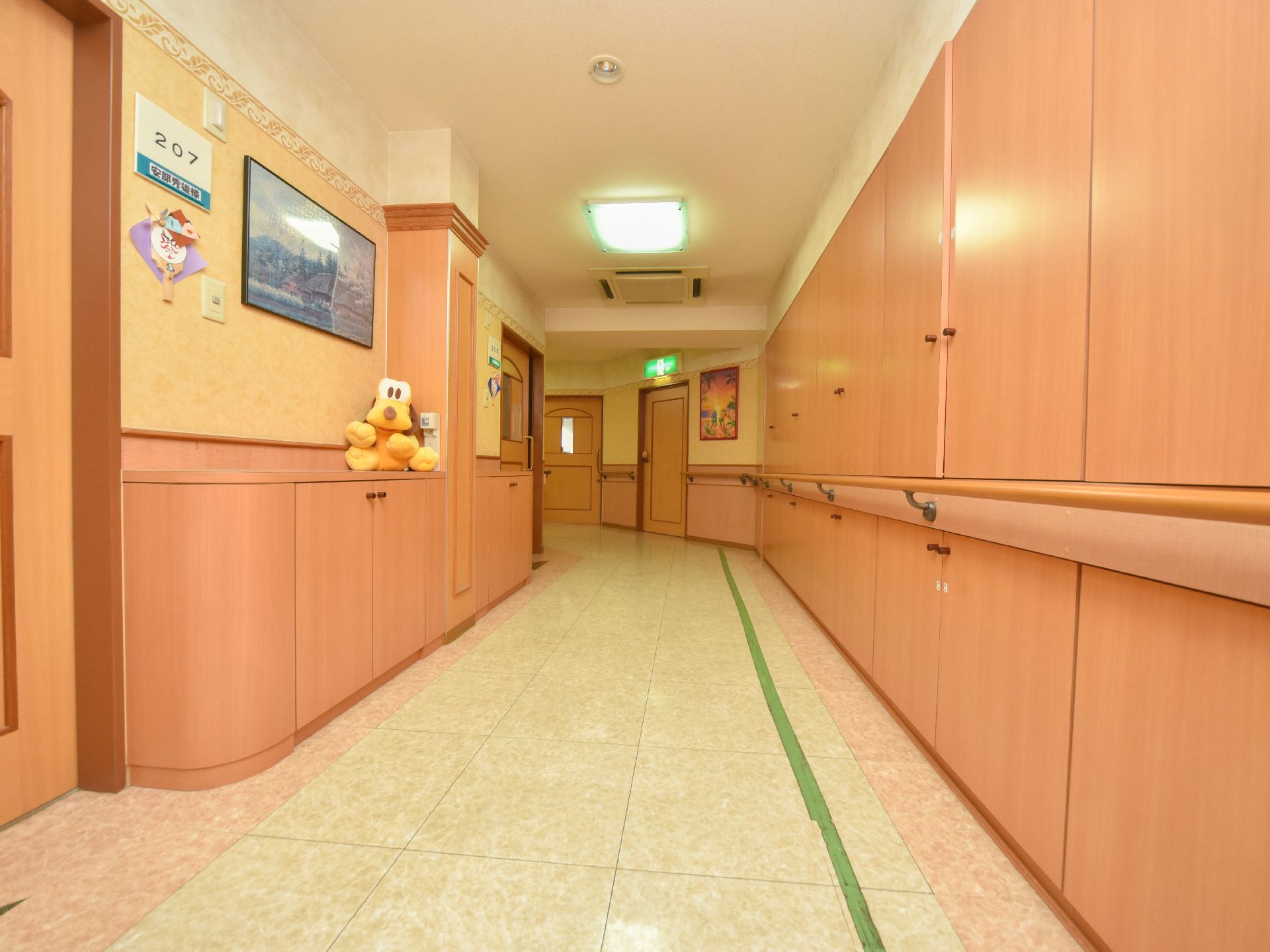 居室前の廊下はとても広く、壁には手すりが設置されている。居室のドアの横には部屋番号と入居者のお名前が表示されている。
