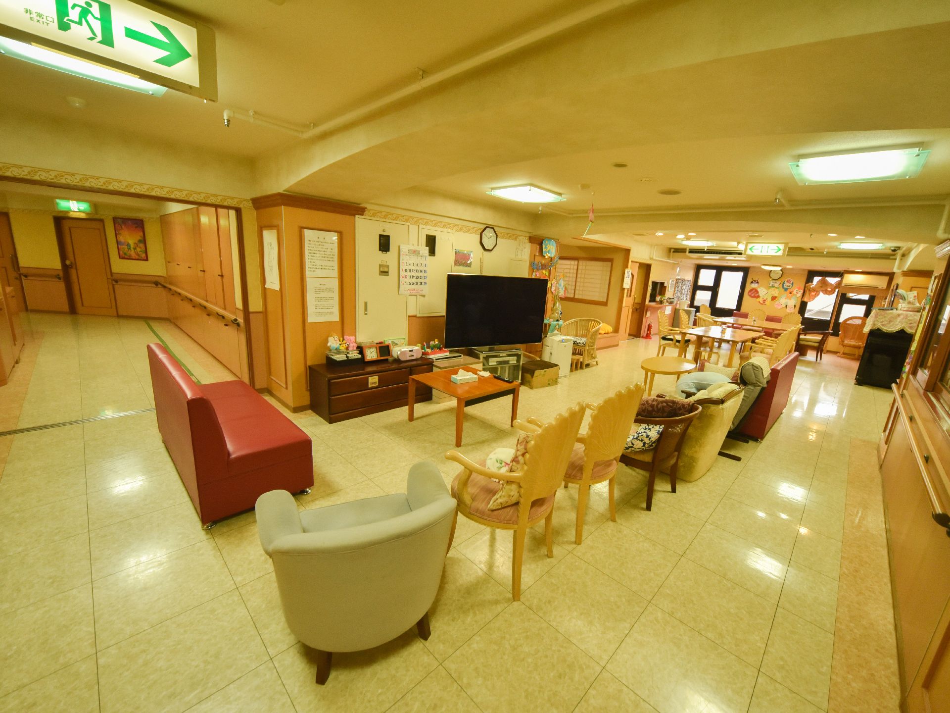 壁際に大きなテレビが設置されている。テレビの前には四角い小さなテーブルがあり、様々な種類のソファーやいすが置かれている。