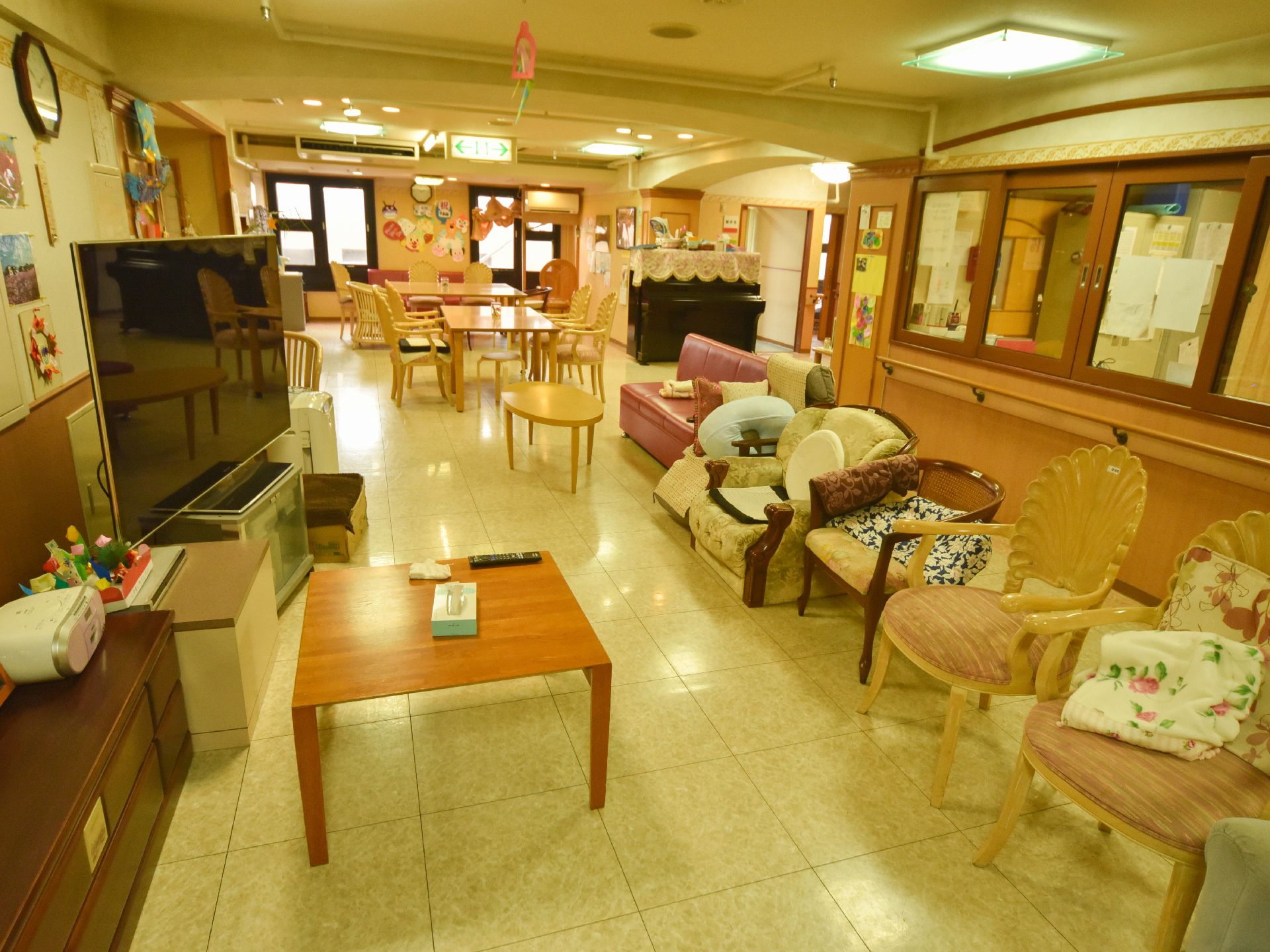 タイプの違う椅子がテレビに向かって複数なんでいる。　壁の一部は収納になっていて、扉は鏡になっている。ピアノも設置されている。