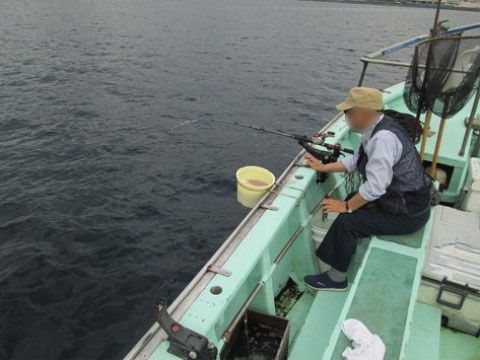 緑色の船の上で釣り竿を垂らし釣りを楽しむ男性